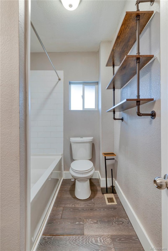 6660 Locust St, Commerce City, CO 80022 - bathroom featuring toilet, a textured ceiling, wood finished floors, baseboards, and bathtub / shower combination