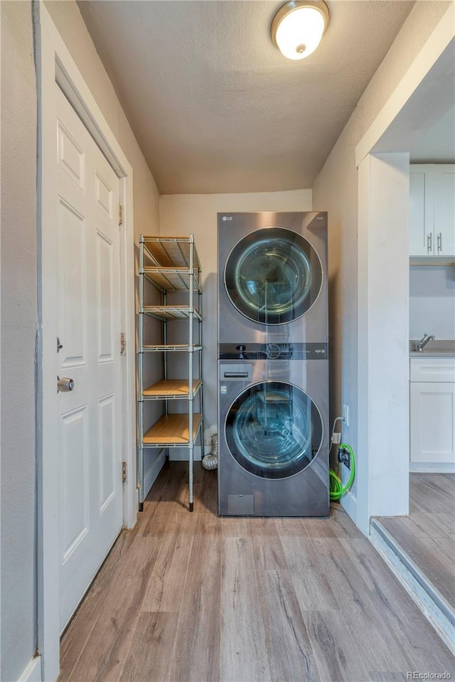6660 Locust St, Commerce City, CO 80022 - clothes washing area with stacked washer and clothes dryer, a textured ceiling, and wood finished floors