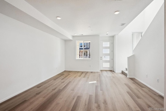 unfurnished living room featuring visible vents, stairway, light wood-style flooring, and baseboards