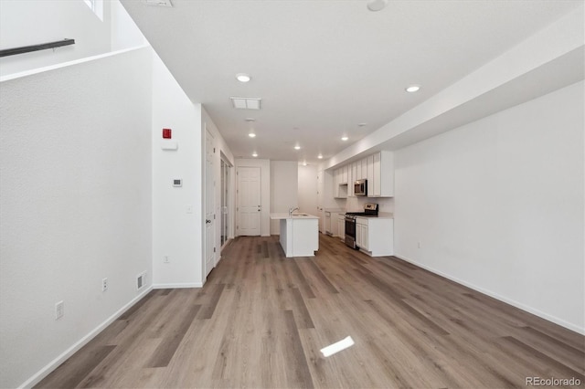 unfurnished living room featuring visible vents, a sink, recessed lighting, light wood-style floors, and baseboards