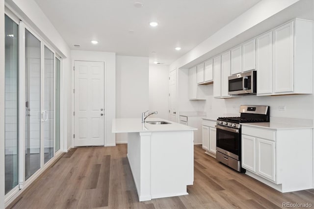 kitchen with a kitchen island with sink, a sink, white cabinets, light wood-style floors, and appliances with stainless steel finishes