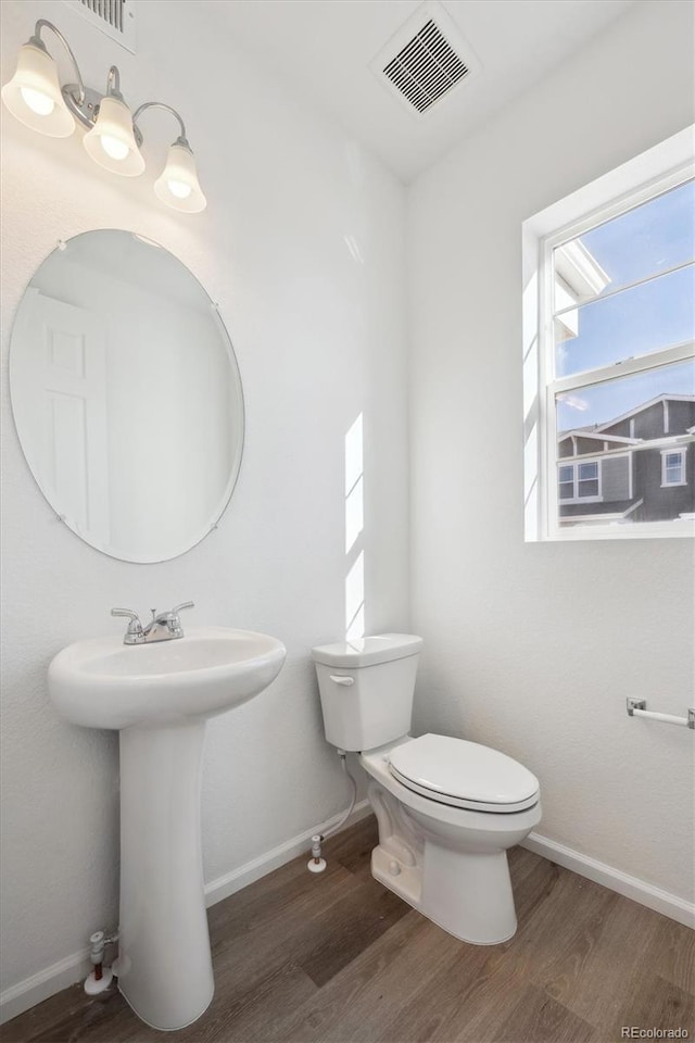 half bath with visible vents, toilet, baseboards, and wood finished floors