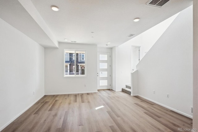 unfurnished living room featuring visible vents, baseboards, light wood-style flooring, and stairway