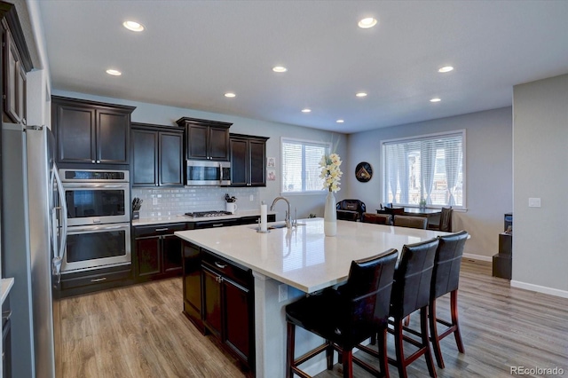 kitchen with appliances with stainless steel finishes, sink, backsplash, a kitchen bar, and a kitchen island with sink