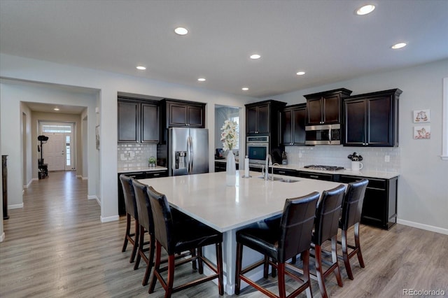 kitchen with a kitchen bar, sink, light wood-type flooring, appliances with stainless steel finishes, and a kitchen island with sink