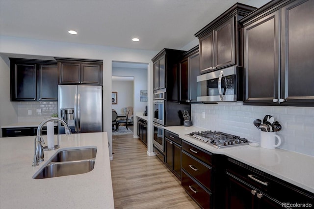 kitchen featuring dark brown cabinetry, sink, appliances with stainless steel finishes, light hardwood / wood-style floors, and backsplash