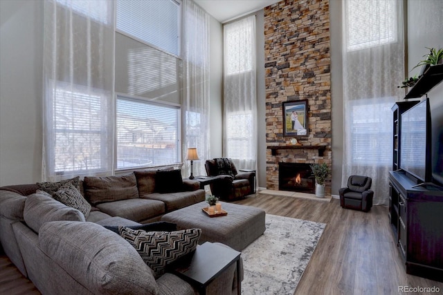 living room with a stone fireplace, light hardwood / wood-style floors, and a high ceiling