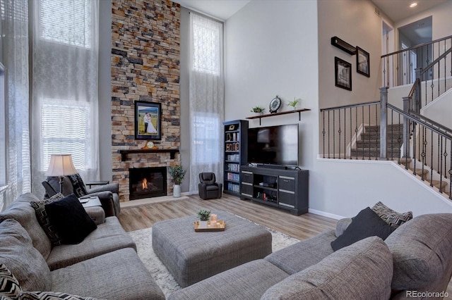 living room with a high ceiling, a stone fireplace, and light hardwood / wood-style floors