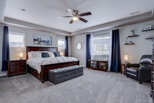 bedroom featuring multiple windows, light colored carpet, a raised ceiling, and ceiling fan