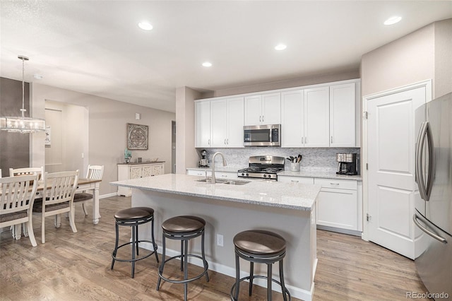 kitchen featuring a center island with sink, sink, hanging light fixtures, white cabinetry, and stainless steel appliances