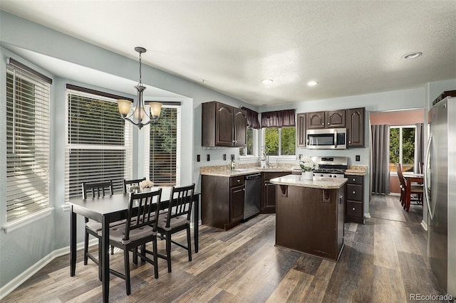 kitchen featuring pendant lighting, dark wood-type flooring, appliances with stainless steel finishes, a center island, and an inviting chandelier