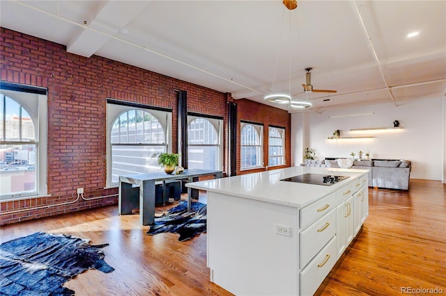 1555 California St Unit 605, Denver, CO 80202 - kitchen featuring brick wall, black electric cooktop, plenty of natural light, white cabinets, and light wood-style flooring