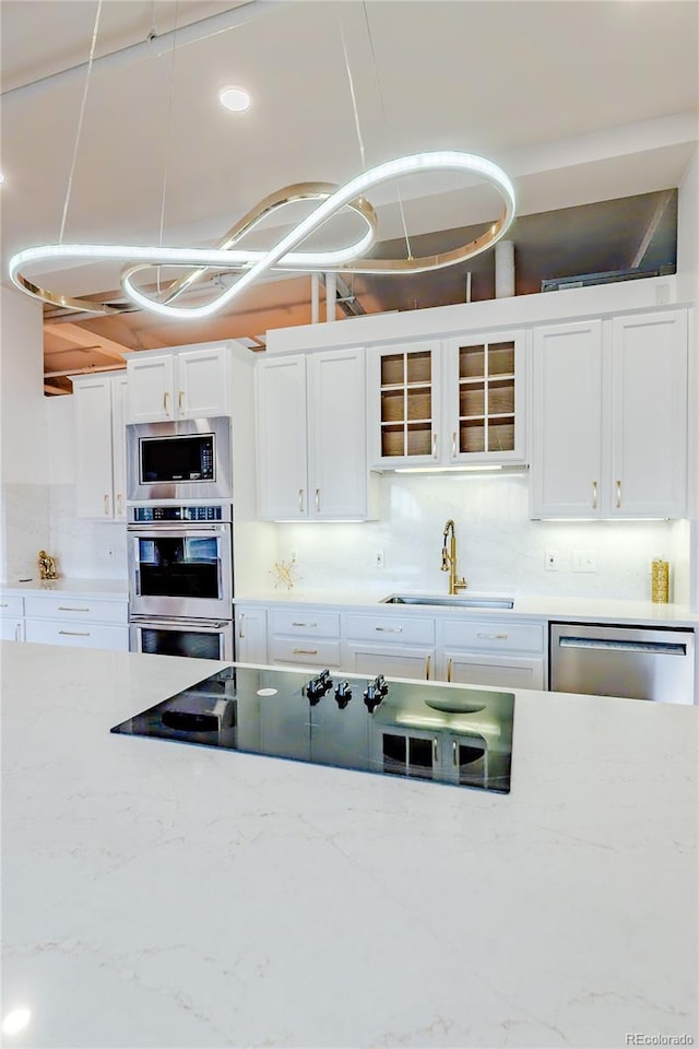 1555 California St Unit 605, Denver, CO 80202 - kitchen featuring a sink, appliances with stainless steel finishes, white cabinets, glass insert cabinets, and light stone counters