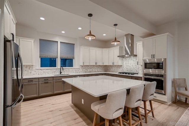 kitchen featuring a center island, decorative light fixtures, stainless steel appliances, a sink, and wall chimney range hood