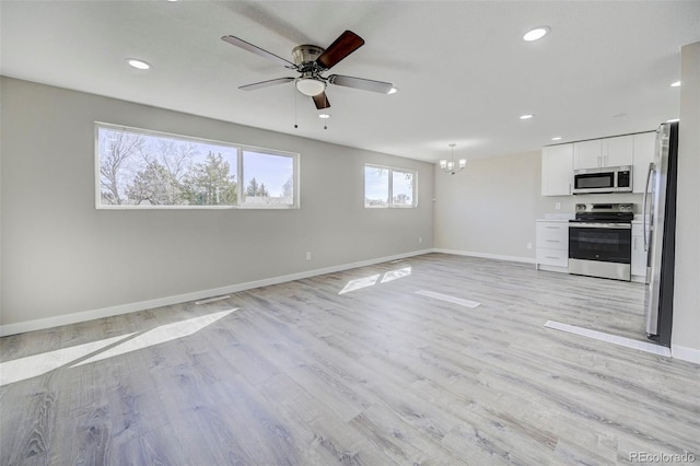 unfurnished living room with ceiling fan with notable chandelier, light wood-type flooring, and baseboards