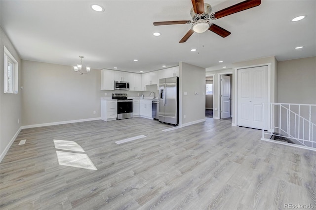 unfurnished living room featuring baseboards, recessed lighting, ceiling fan with notable chandelier, light wood-type flooring, and a wealth of natural light