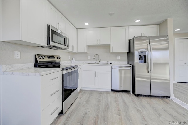 kitchen with white cabinets, stainless steel appliances, light wood-style flooring, and a sink