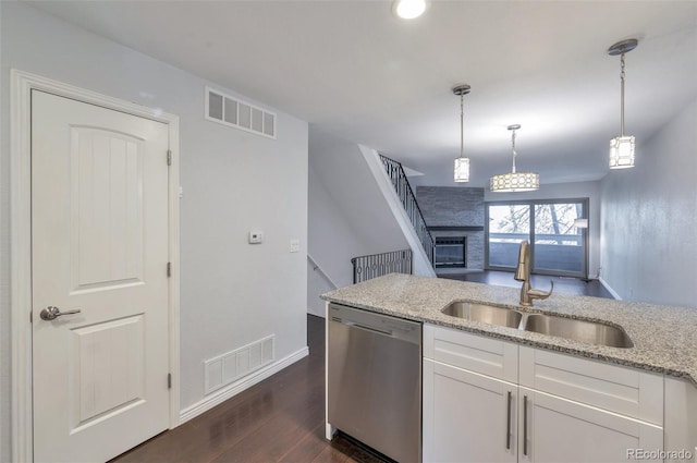 kitchen with decorative light fixtures, white cabinetry, sink, stainless steel dishwasher, and light stone counters