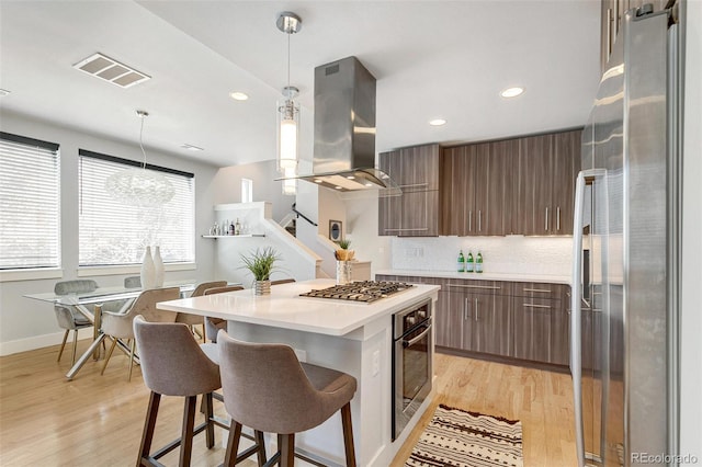 kitchen featuring decorative light fixtures, light wood-type flooring, island exhaust hood, and appliances with stainless steel finishes