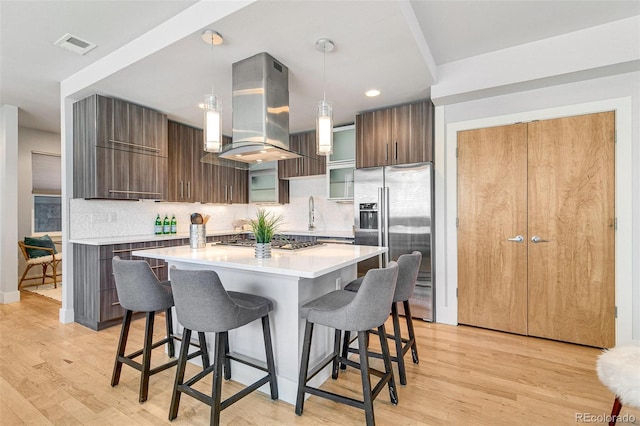 kitchen with a breakfast bar, pendant lighting, island exhaust hood, a center island, and stainless steel appliances