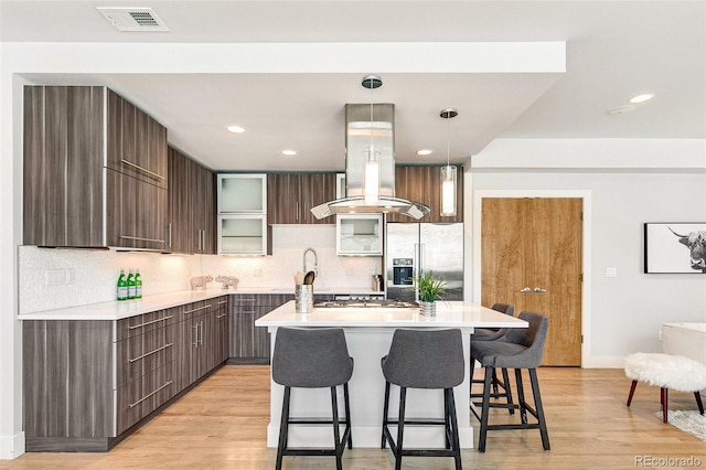 kitchen with hanging light fixtures, island exhaust hood, appliances with stainless steel finishes, and a kitchen island