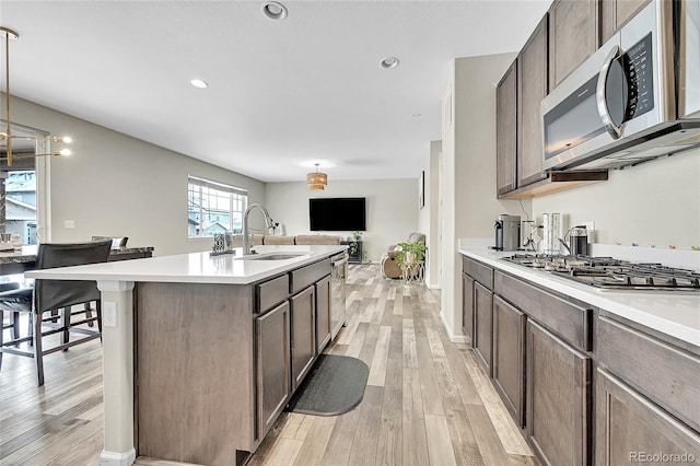 kitchen with a center island with sink, appliances with stainless steel finishes, decorative light fixtures, light countertops, and a sink