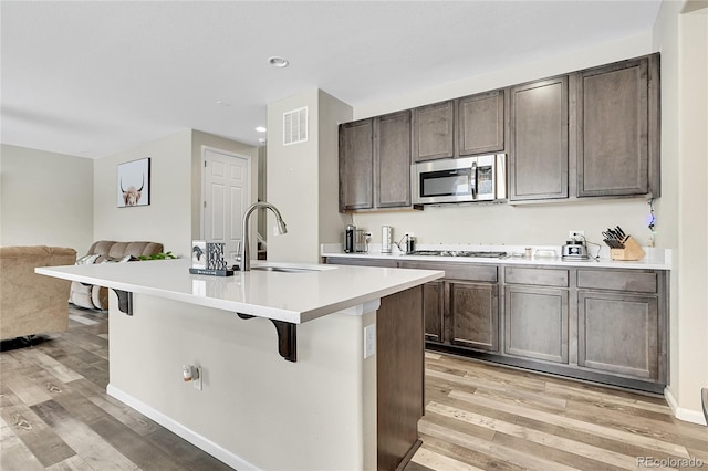 kitchen featuring light countertops, appliances with stainless steel finishes, a kitchen island with sink, a sink, and a kitchen bar