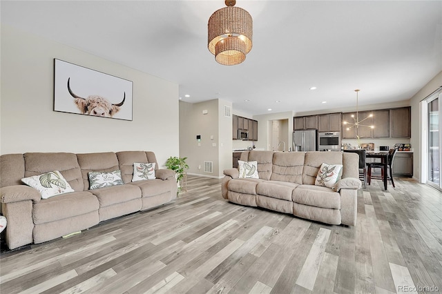 living room featuring a chandelier, light wood-type flooring, visible vents, and recessed lighting