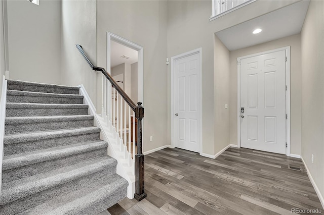 foyer entrance featuring dark wood-style flooring, a high ceiling, baseboards, and stairs