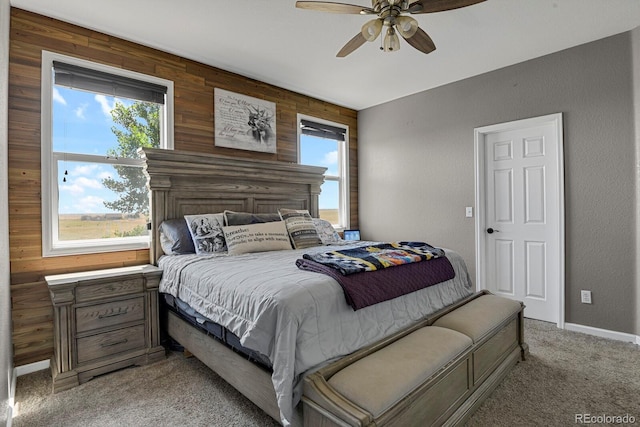 carpeted bedroom featuring ceiling fan, wooden walls, and multiple windows