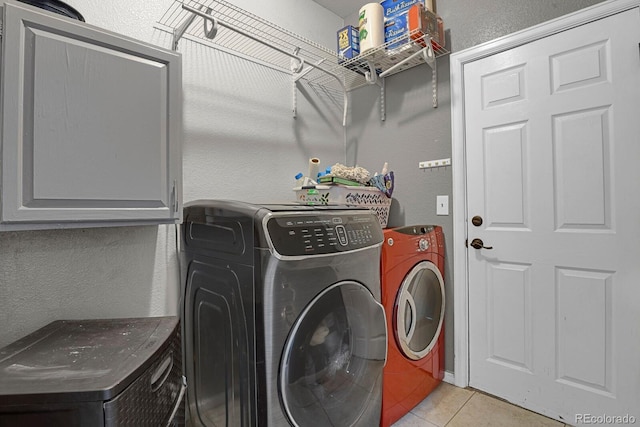 laundry room featuring washing machine and dryer, light tile patterned flooring, and cabinets