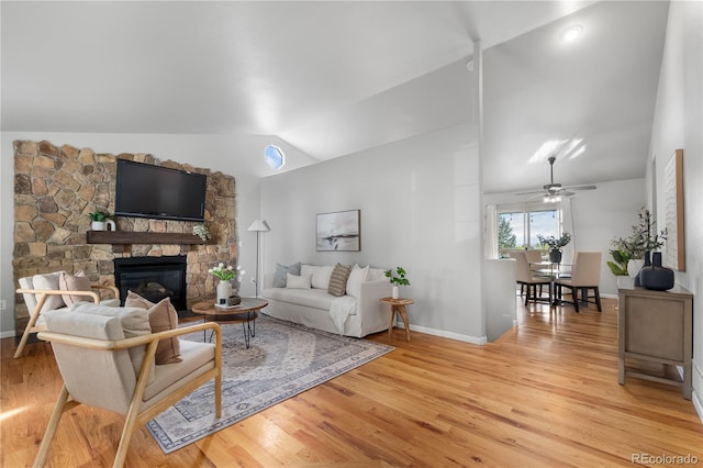 living room with a stone fireplace, vaulted ceiling, and light hardwood / wood-style floors