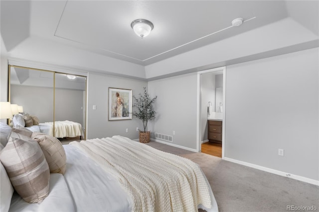 bedroom featuring ensuite bath, carpet flooring, a raised ceiling, and a closet