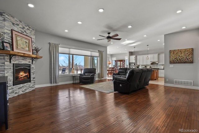 living room featuring ceiling fan, a fireplace, and dark wood-type flooring