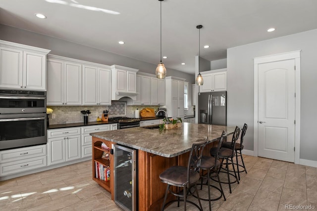 kitchen with white cabinetry, a center island with sink, beverage cooler, and appliances with stainless steel finishes