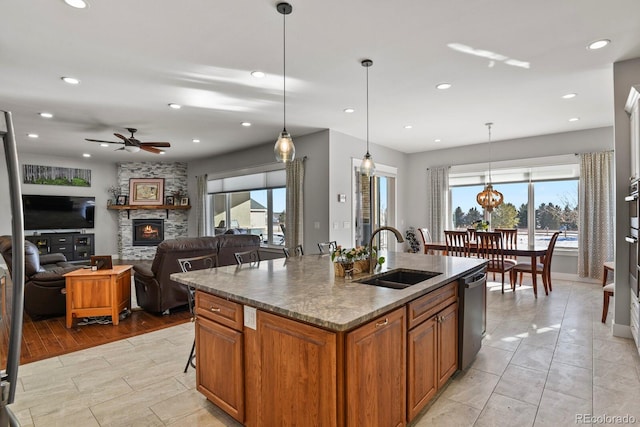 kitchen featuring ceiling fan, sink, a stone fireplace, an island with sink, and pendant lighting