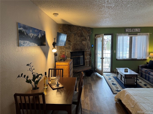 bedroom with a textured ceiling, a textured wall, a fireplace, wood finished floors, and access to exterior