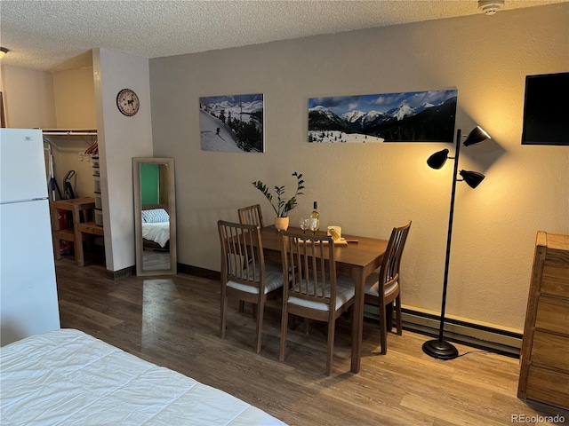 dining area with a textured ceiling, baseboards, and wood finished floors