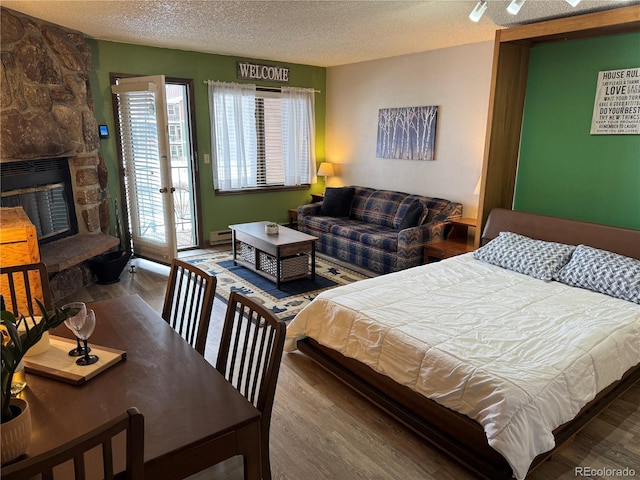 bedroom with a textured ceiling, access to outside, a fireplace, and wood finished floors