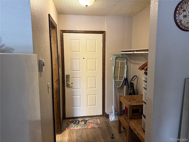 doorway to outside featuring a textured wall, a textured ceiling, and wood finished floors