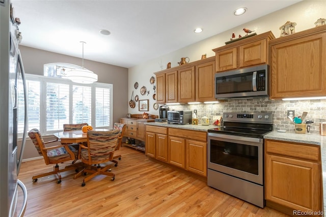 kitchen featuring tasteful backsplash, light stone countertops, hanging light fixtures, stainless steel appliances, and light hardwood / wood-style flooring