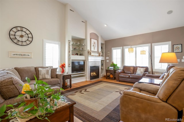 living room with high vaulted ceiling, wood-type flooring, and a tile fireplace