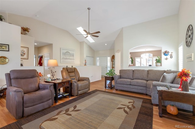 living room featuring high vaulted ceiling, ceiling fan with notable chandelier, and light wood-type flooring