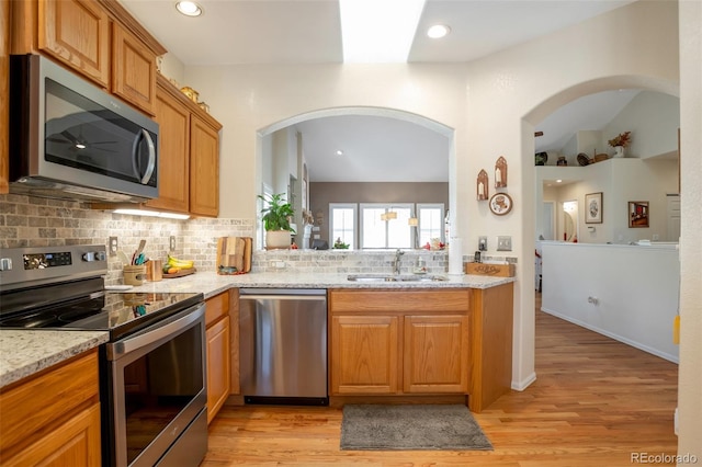 kitchen with tasteful backsplash, light stone countertops, appliances with stainless steel finishes, sink, and light wood-type flooring