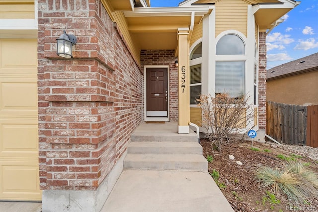 doorway to property with brick siding and fence