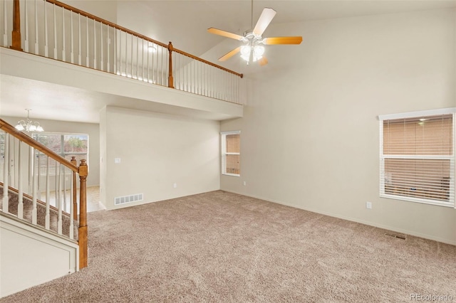 unfurnished living room with a towering ceiling, carpet floors, a chandelier, ceiling fan, and stairway