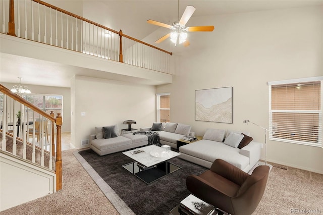living area with carpet floors, a chandelier, a towering ceiling, ceiling fan, and stairs