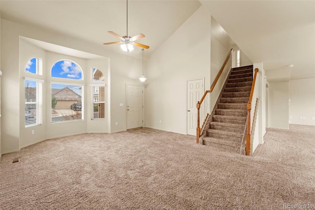 unfurnished living room with high vaulted ceiling, carpet flooring, a ceiling fan, stairs, and baseboards