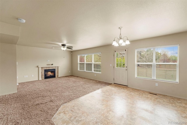 unfurnished living room with ceiling fan, a chandelier, a tile fireplace, and baseboards