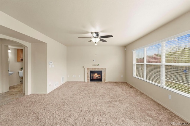 unfurnished living room featuring ceiling fan, a tiled fireplace, light carpet, arched walkways, and baseboards